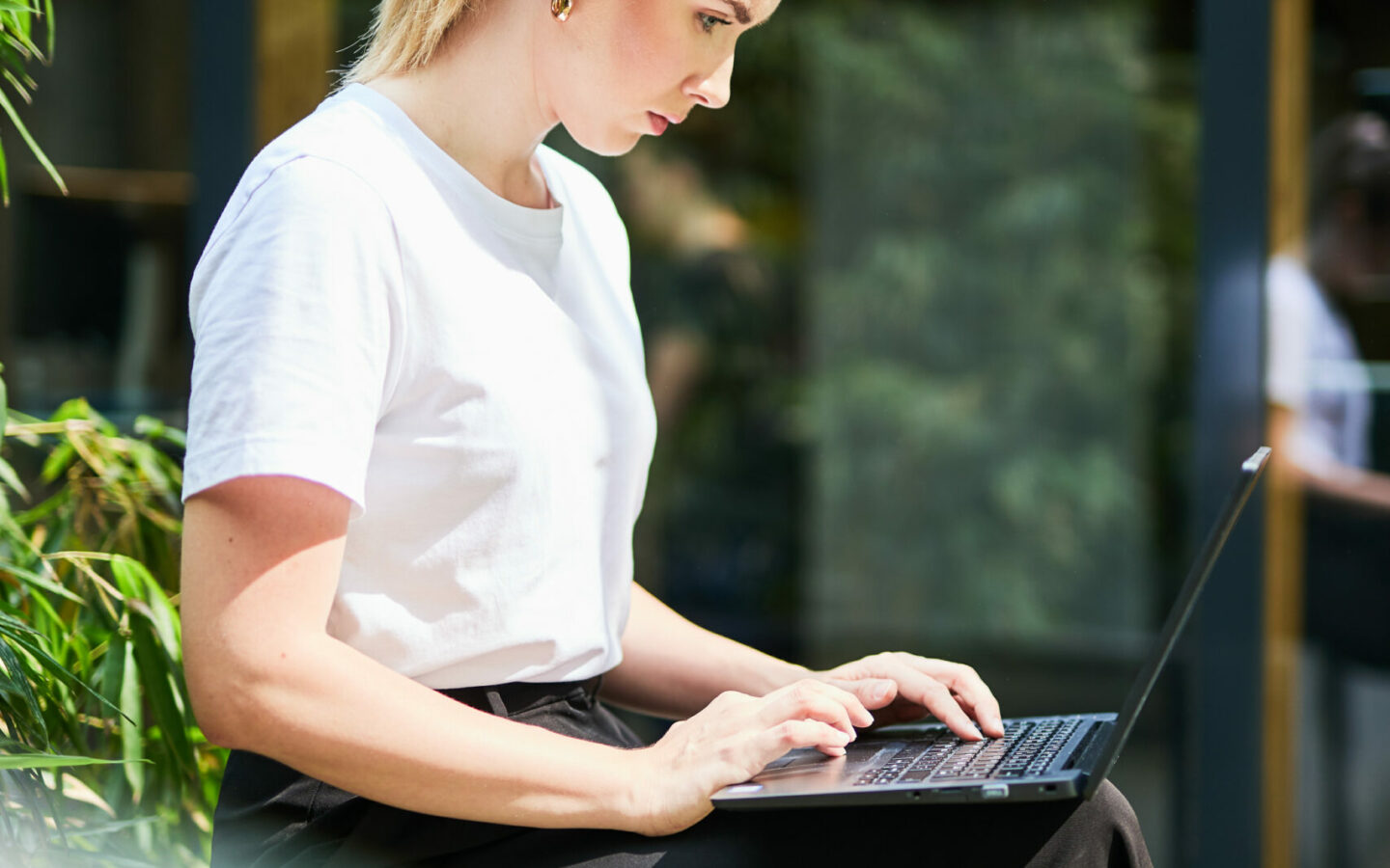 Picture of a woman working on the terrace with her laptop on her lap.