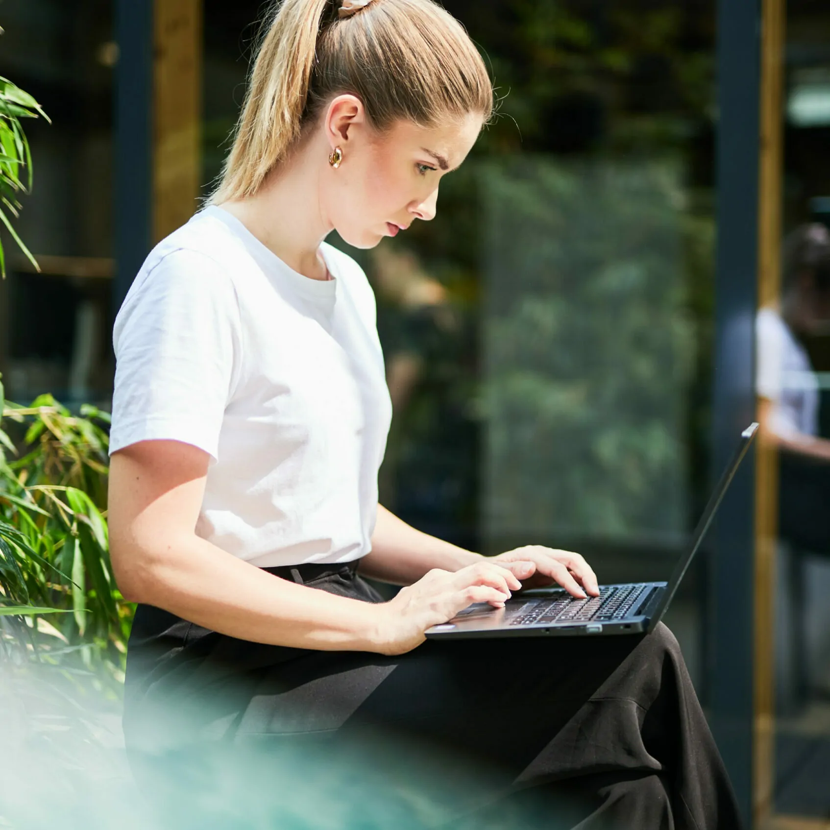 Picture of a woman working on the terrace with her laptop on her lap.