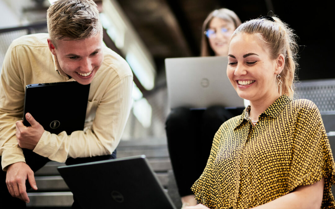 Photo of a young woman and a young man sitting on steps and working on a presentation on a laptop.