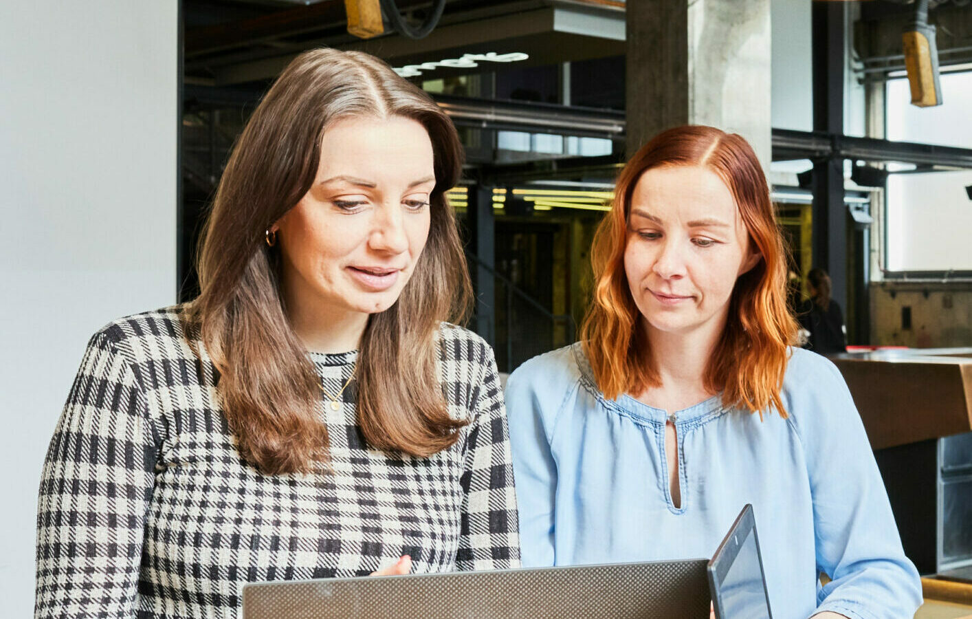 Bild von drei jungen Frauen, die an einem Stehtisch mit Laptop ein kurzes Meeting abhalten.