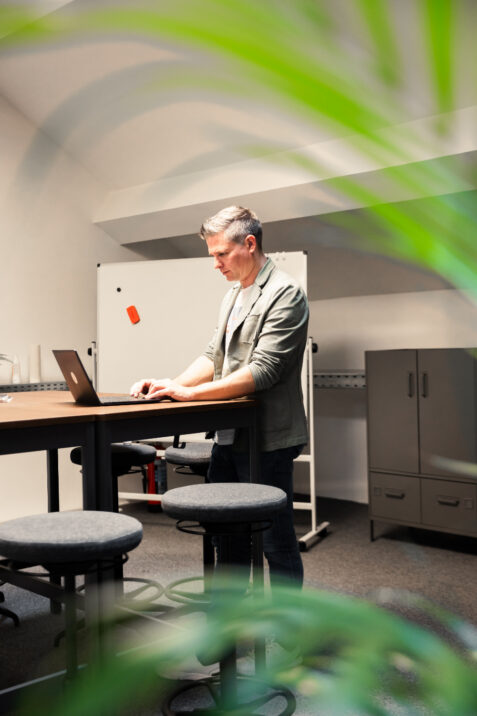 Foto von einem Mann der an einem Stehtisch steht und am Laptop arbeitet.