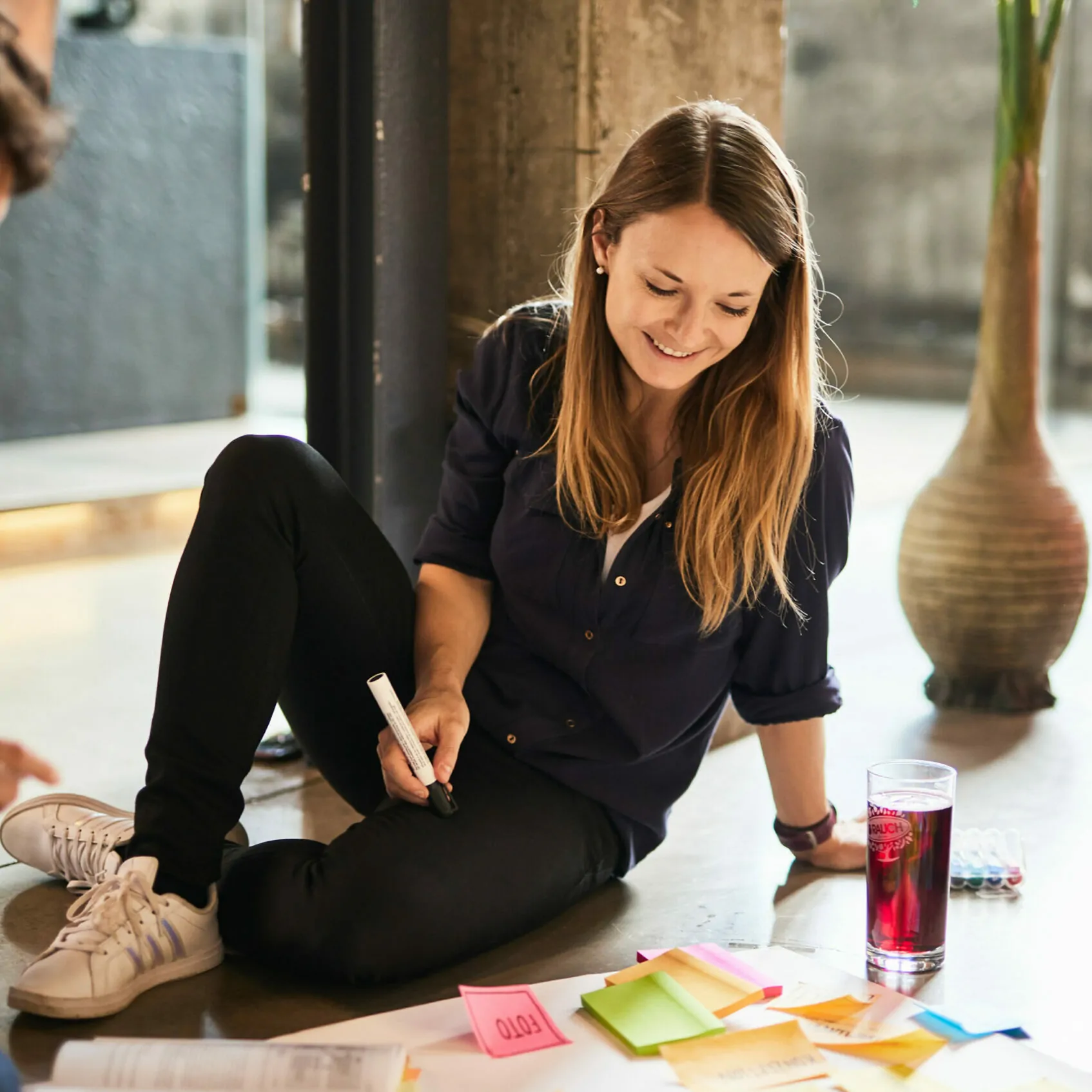 Foto von einer jungen Frau mit einem Stift in der Hand, die am Boden sitzt und an einem Plakat für ein Projekt arbeitet.