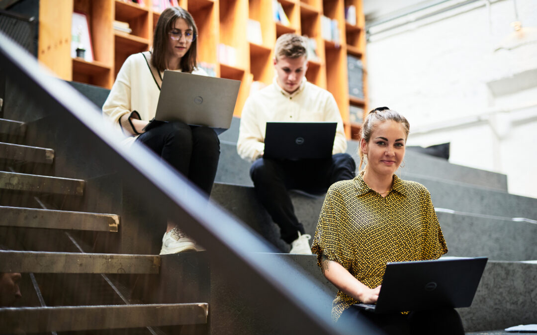 Photo of three colleagues sitting on large steps, working.