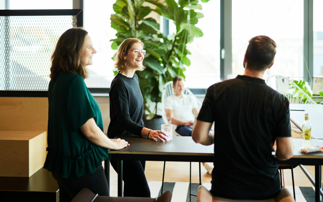 Foto von einer lächelnden Frau, die in zwischen zwei valantic CX Kollegen an einem Bartisch steht.