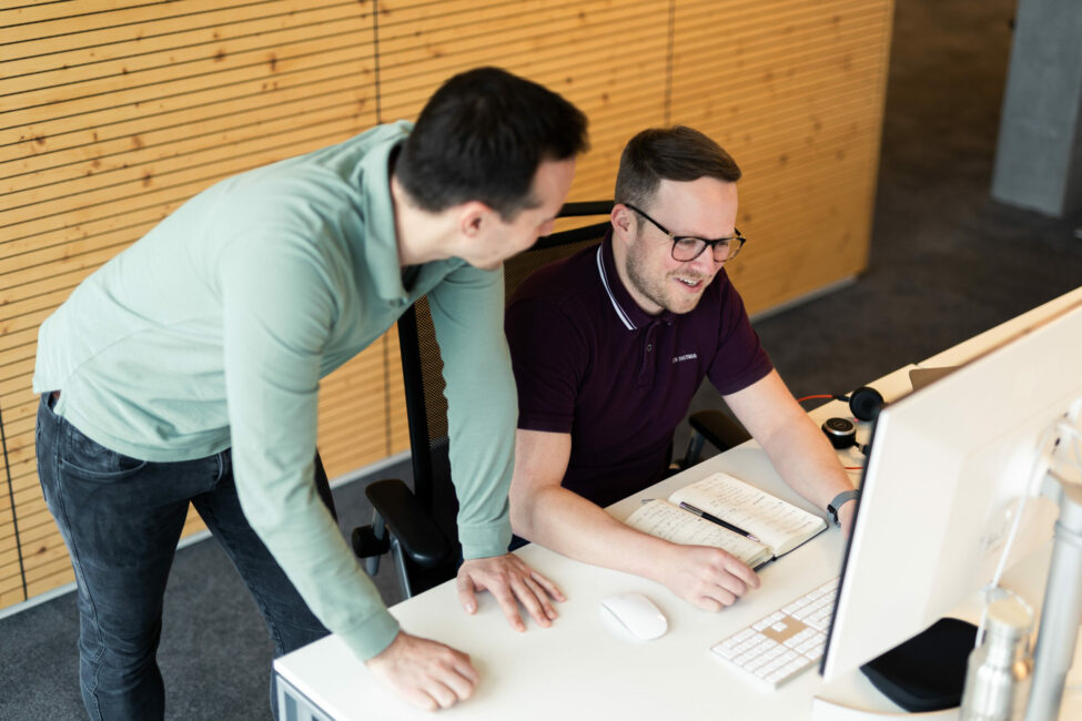 Foto von einer lächelnden Frau und einem Mann, die bei einem Feierabendbier ihren valantic-CX-Kolleg*innen zuhören.