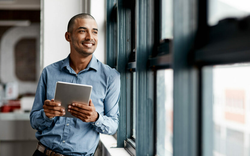 Lächelnder Geschäftsmann mit Tablet in der Hand schaut aus Fenster
