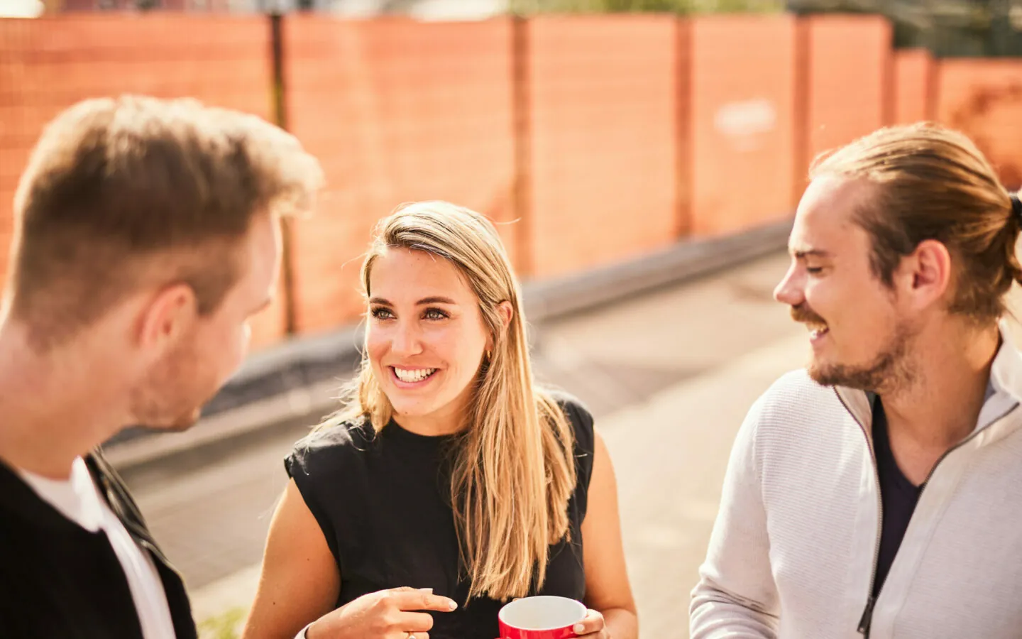 Foto von einer lächelnden Frau mit einer Kaffeetasse, die sich mit ihren beiden CX-Mitarbeitern über Customer Experience unterhält.