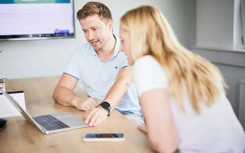 Bild von einem valantic CX-Mitarbeiter, der seiner Kollegin am Laptop aktuelle Daten einer Customer Journey erklärt.