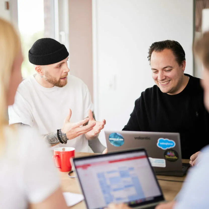 Photo of a staff meeting in which a valantic CX employee is gesturing with his hands, explaining something to his colleague.