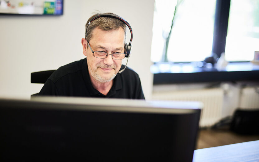 Foto von einem älteren valantic-CX-Mitarbeiter, der Kopfhörer trägt und konzentriert am Computer arbeitet.