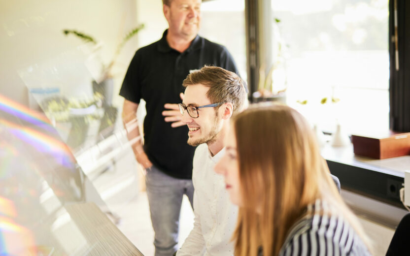 Produktdatenmanagement - Drei Personen in einem Meeting in einem lichtdurchfluteten Meetingraum.