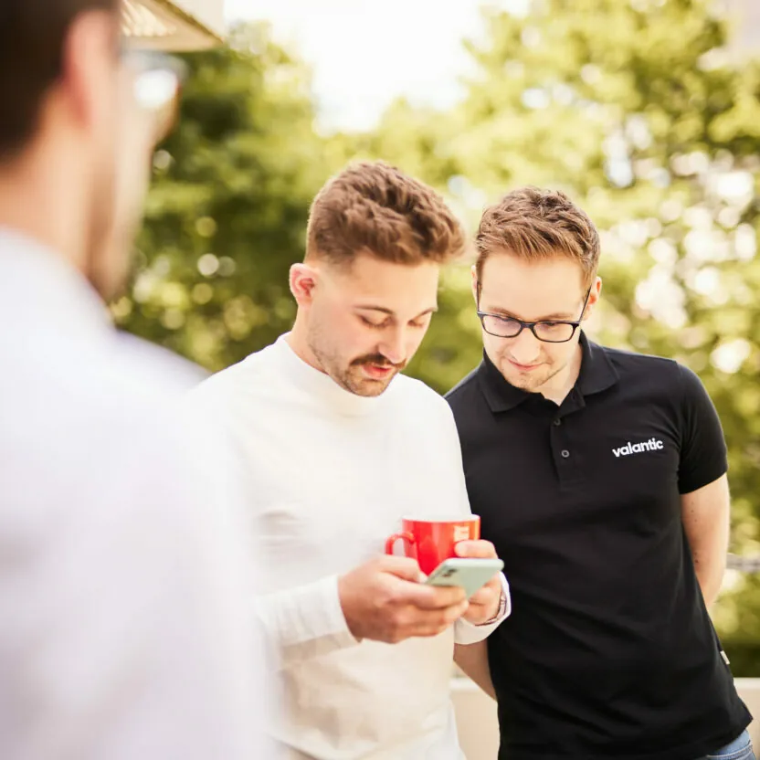 Photo of two valantic CX employees checking out the new customer website on a smartphone.