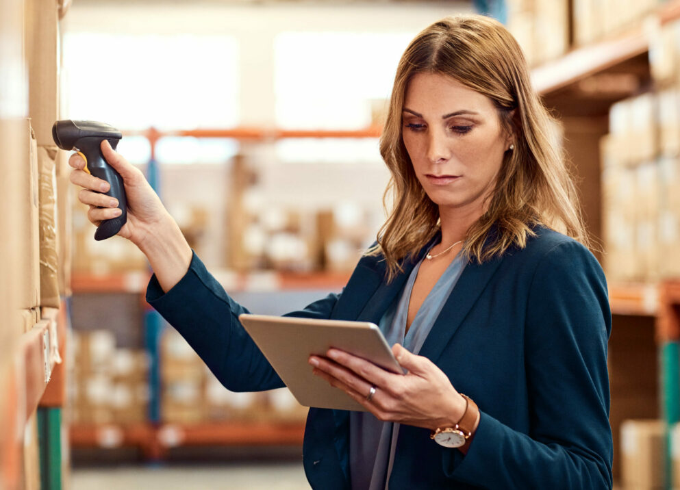 Woman scans goods in warehouse and looks at tablet | procurement record in SAP