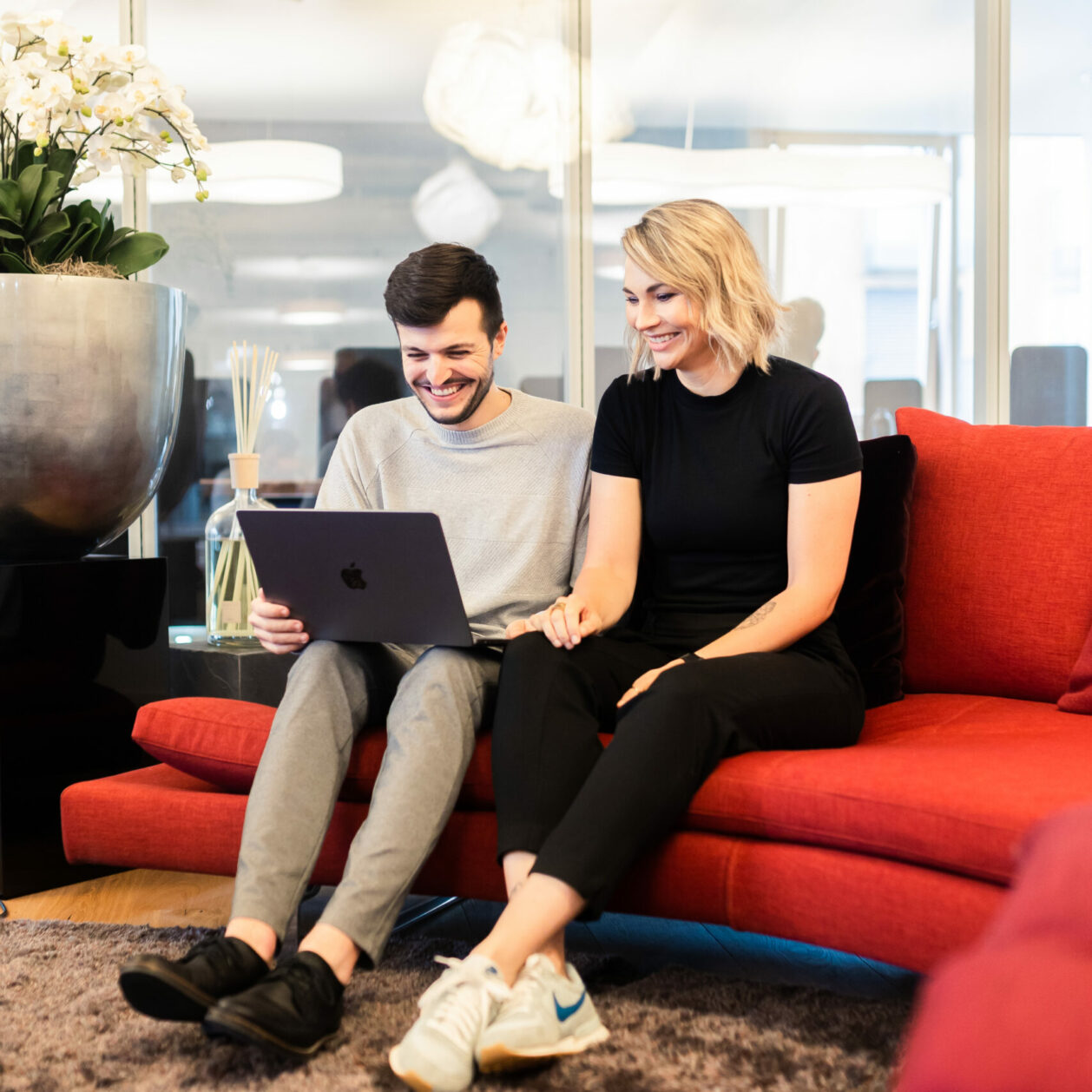 Zwei valantic-CX-Mitarbeiter*innen, die zusammen auf einem Sofa sitzen und in ein Customer-Experience-Präsentation an einem Laptop anschauen.