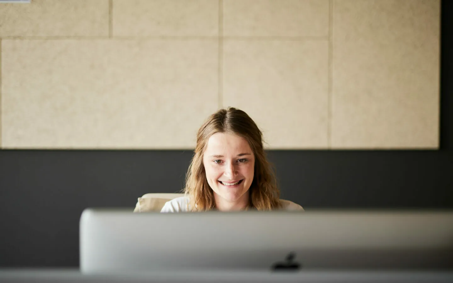Foto von einer jungen, lächelnden Frau, die am PC arbeitet.