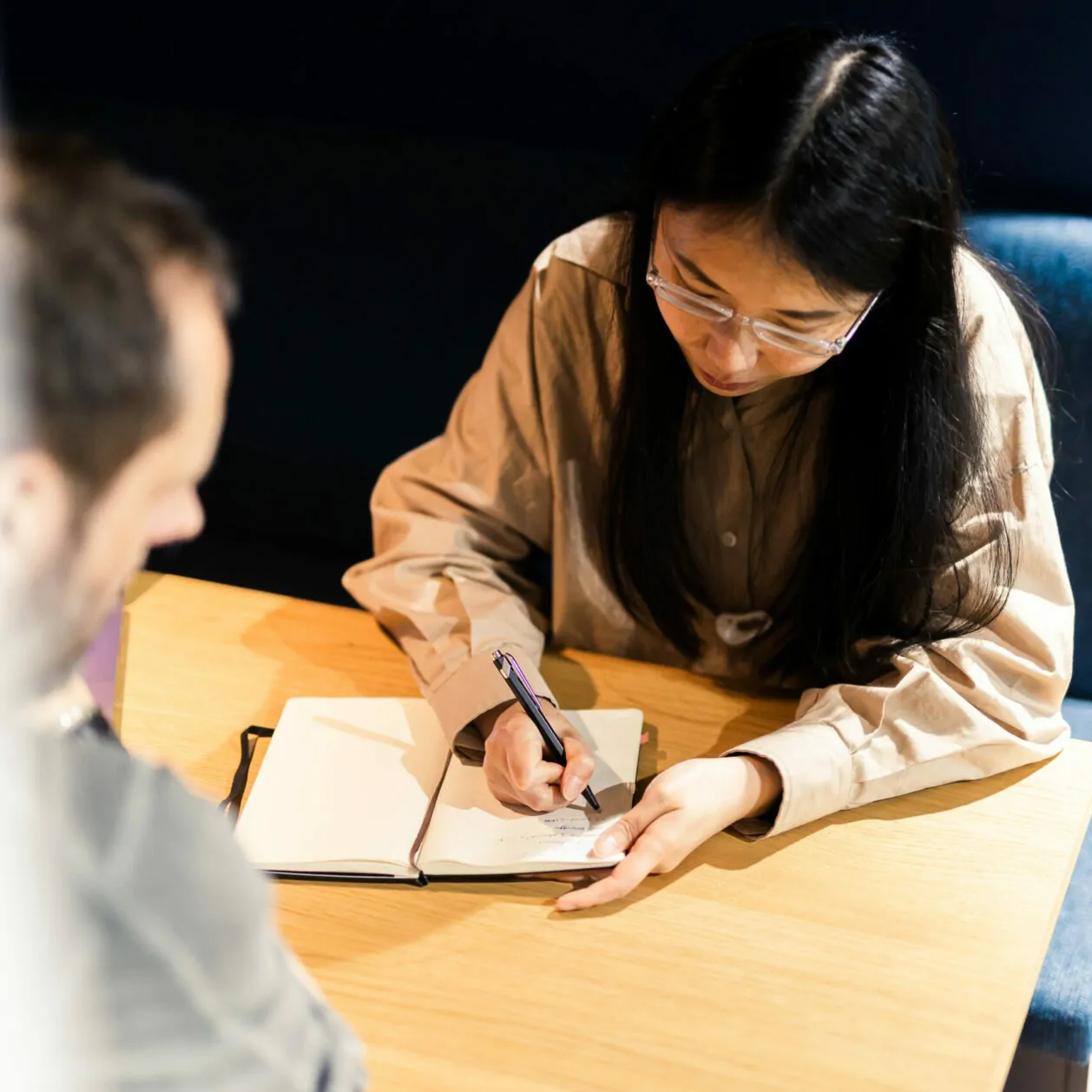 Aufnahme von schräg oben, das eine junge Frau zeigt, die sich in einem Buch Notizen zur Customer Journey eines Kunden macht – valantic CX.
