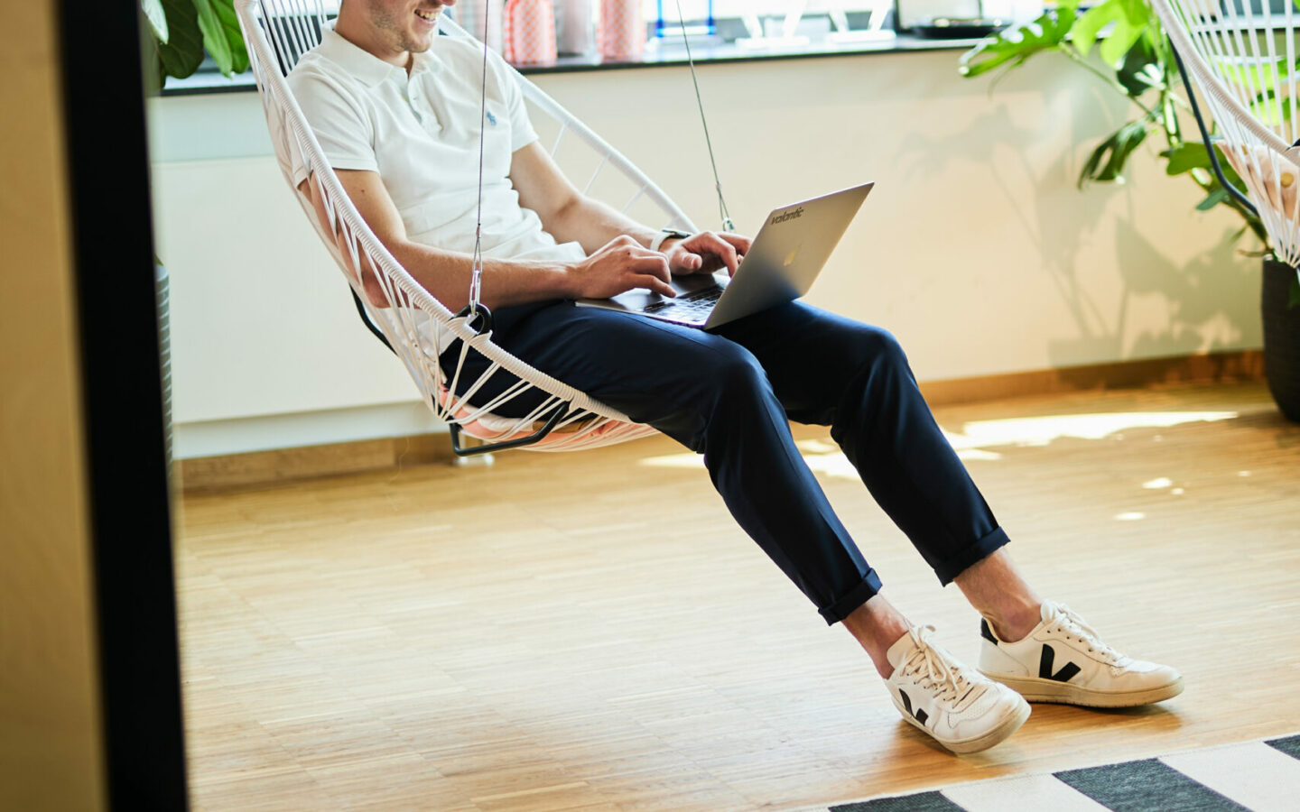Foto von einem valantic-CX-Mitarbeiter, der in einer Sitzschaukel sitzt, den Laptop auf den Oberschenkeln balanciert und E-Mails beantwortet.