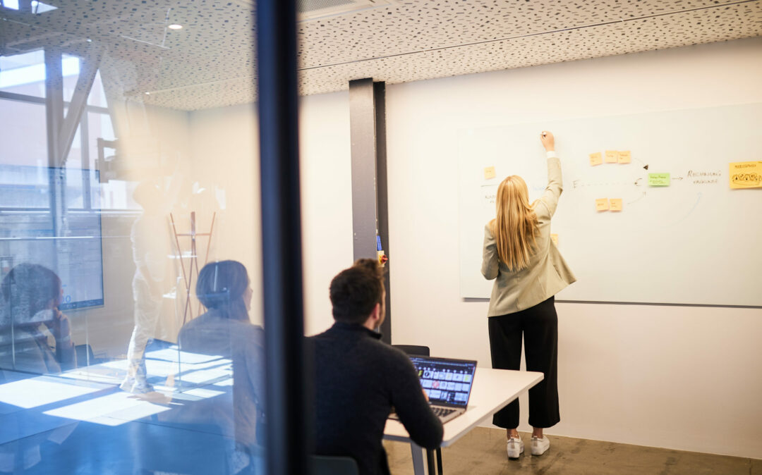 Foto von einer jungen Frau, die während eines Meetings "Customer Experience" auf das Whiteboard schreibt.