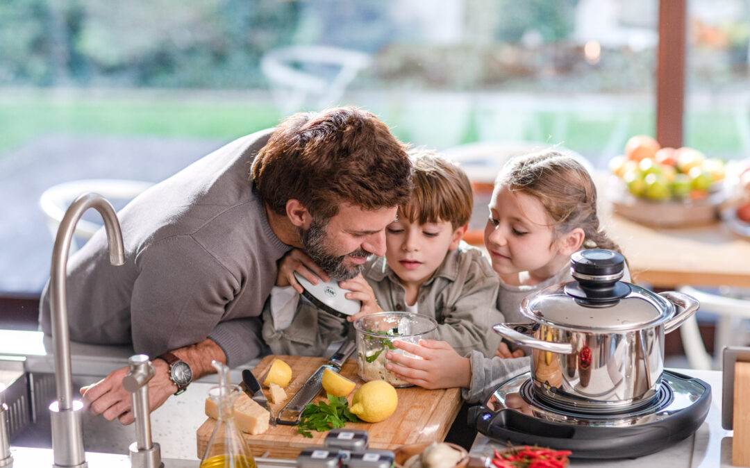Foto von einem Mann mit seinen beiden Kindern beim Kochen in der Küche.