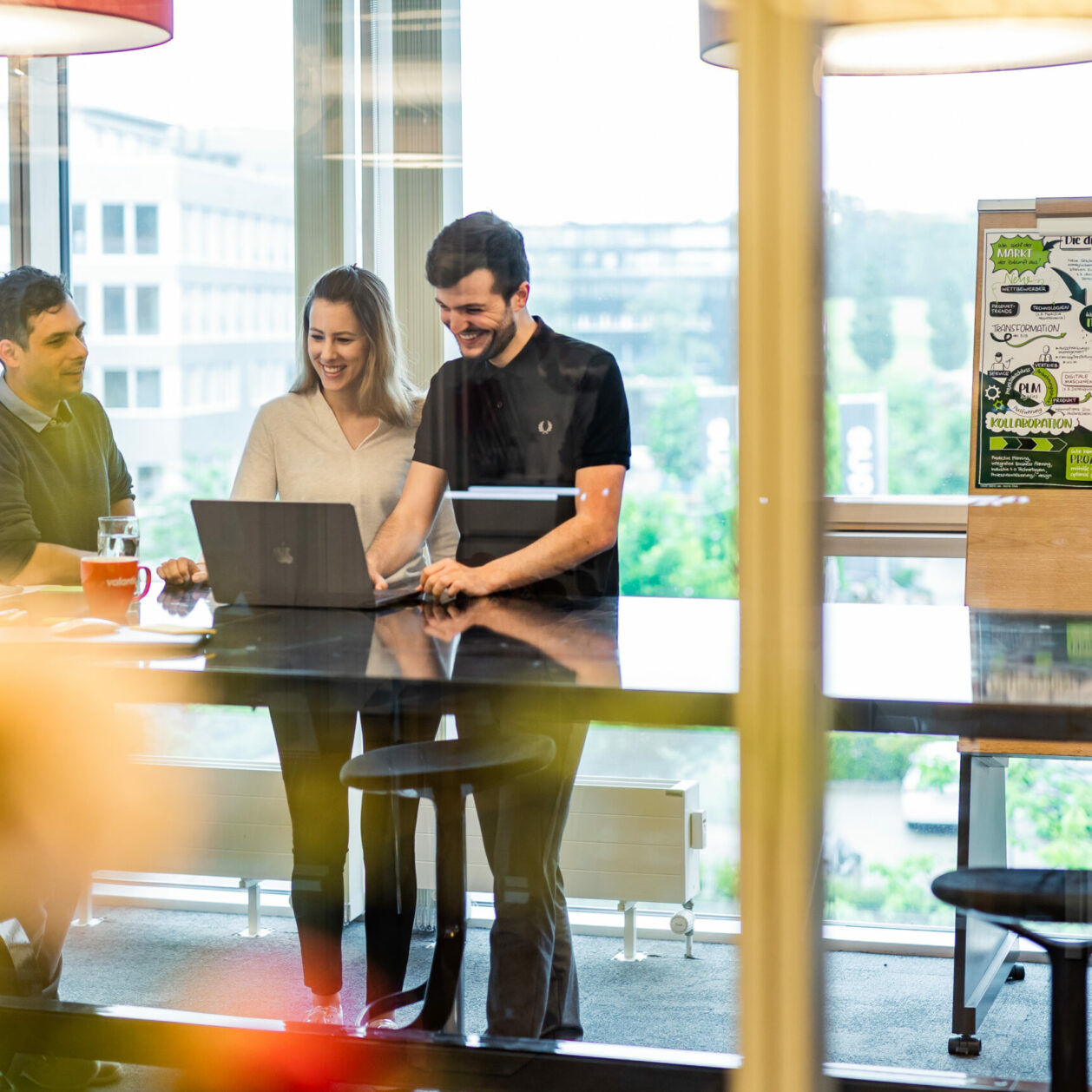 Foto von drei Kolleg:innen, die an einem Steharbeitsplatz stehen und zusammen an einer Customer-Experience-Strategie arbeiten.