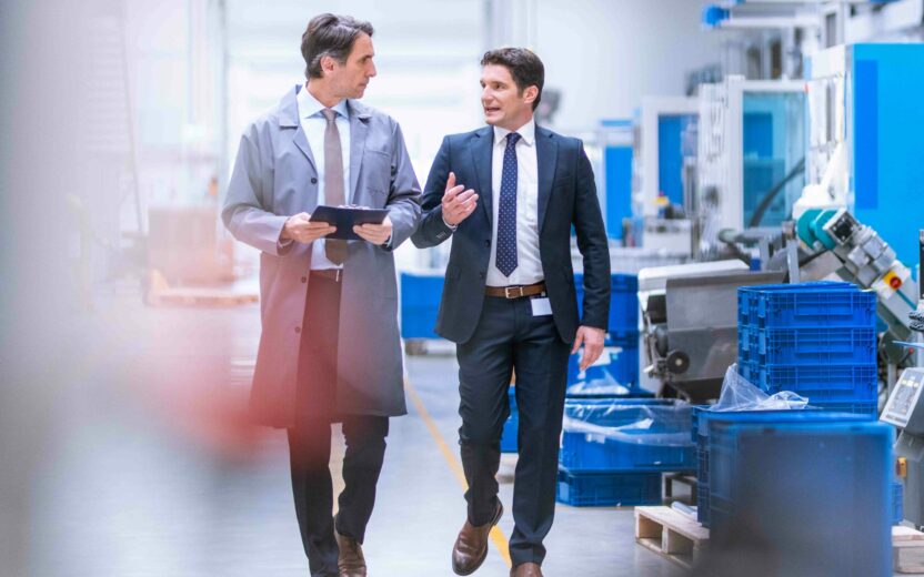 Zwei Männer laufen durch eine Produktionshalle und unterhalten sich