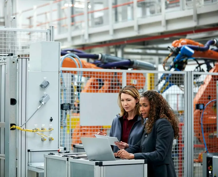 Two women are talking in a production hall and looking at a laptop
