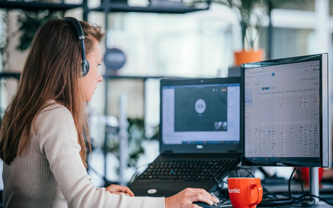 Vrouw die aan haar bureau werkt en een headset draagt terwijl ze naar haar scherm kijkt