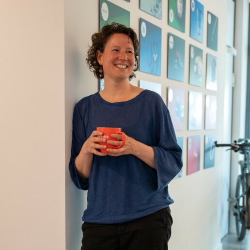 Eine Frau lehnt sich lächelnd an eine Wand mit einer valantic Tasse in den Händen