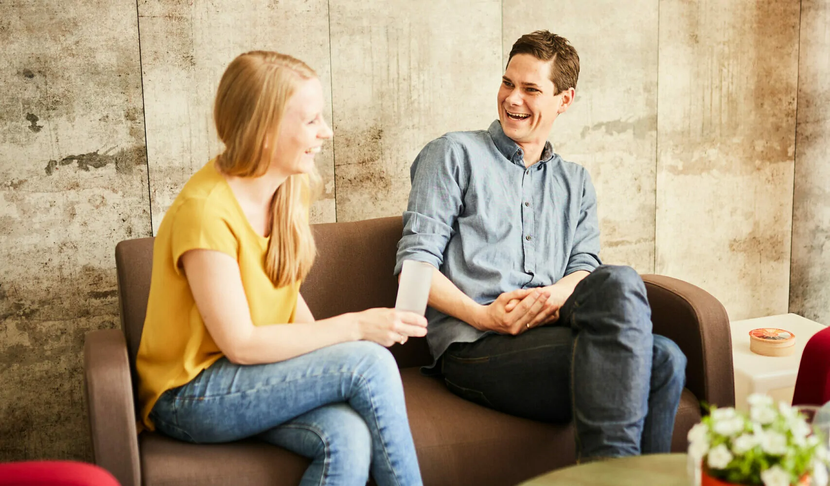 eine junge Frau und ein junger Mann unterhalten sich im Büro auf einem kleinen Sofa