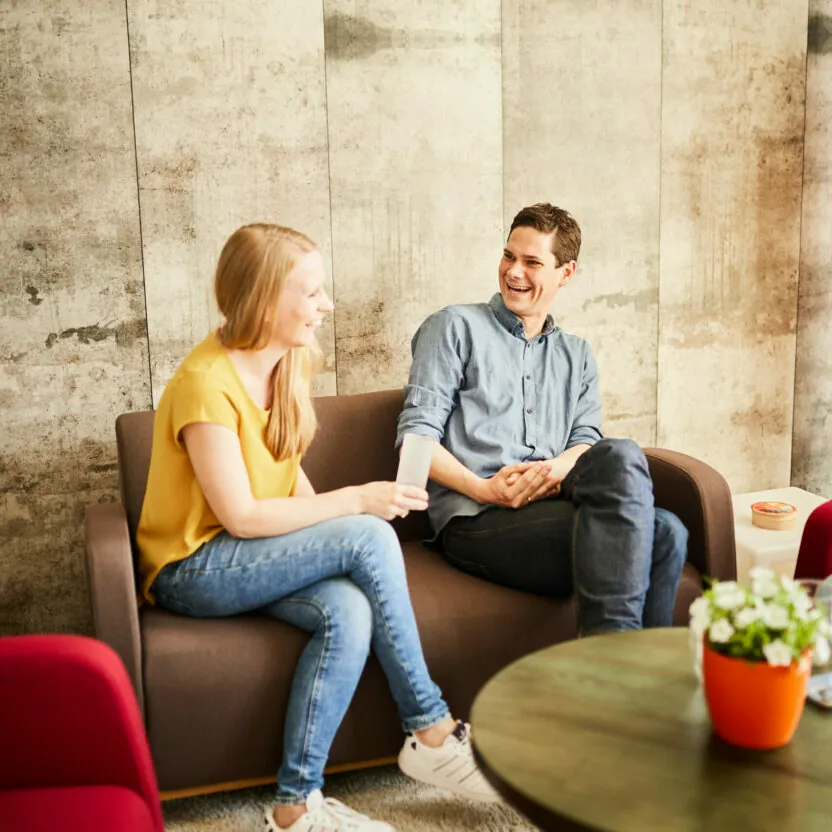 eine junge Frau und ein junger Mann unterhalten sich im Büro auf einem kleinen Sofa