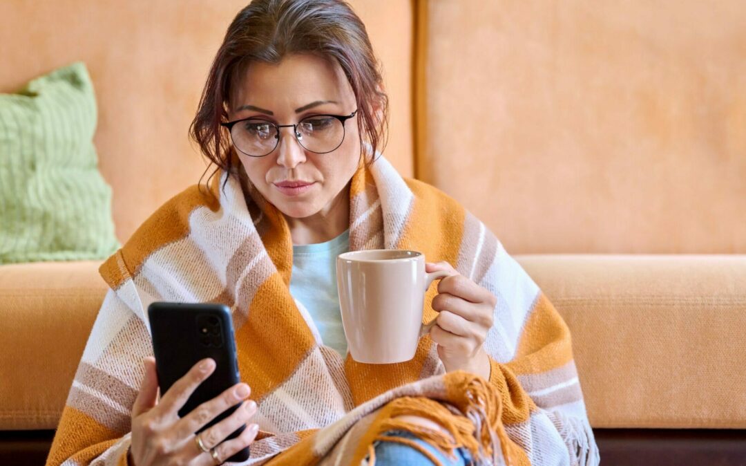 Woman looking at electronic sick note with blanket over her shoulders and cup in hand HCM Inside eAU | valantic SAP