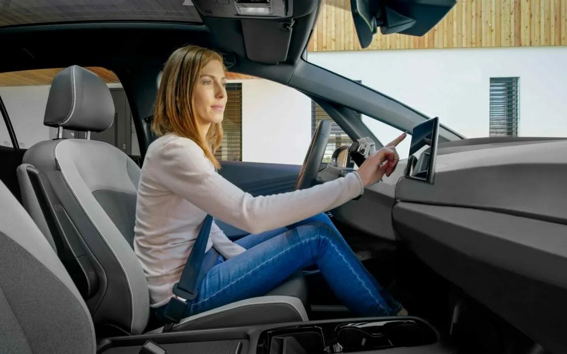 Side view of woman smiling and sitting while touching device screen in modern car.