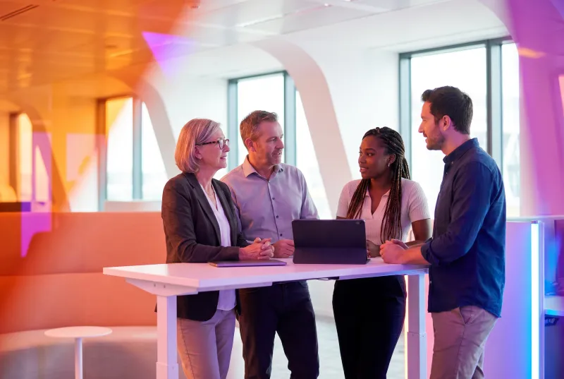 Four colleagues stand around a standing desk discussing work on a tablet in a modern office