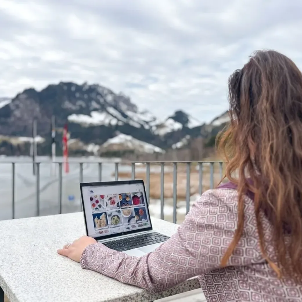 A woman uses her laptop while relaxing on a balcony.