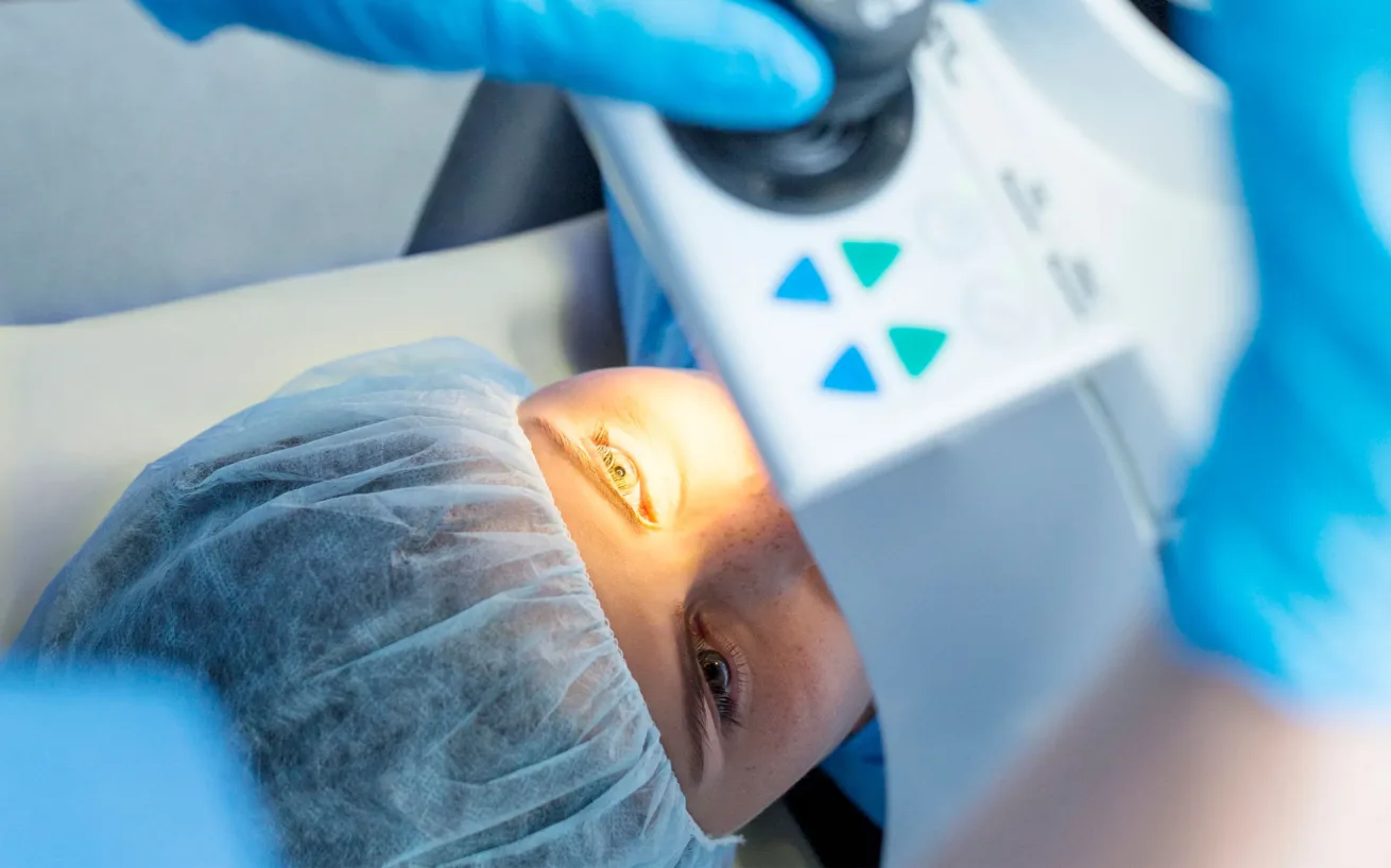 Ein Patient liegt während einer Augenuntersuchung oder eines Eingriffs unter einem medizinischen Gerät, wobei ein helles Licht auf sein offenes Auge gerichtet ist.