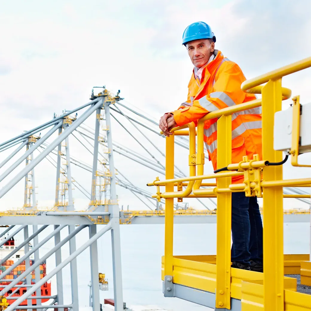 Portrait of a man in workwear standing on a walkway looking out over at a large commercial dock