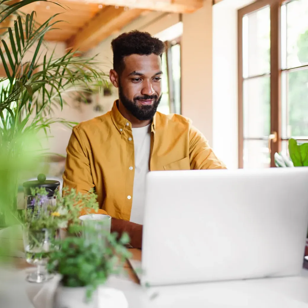 A young man with laptop and coffee working indoors, home office concept.