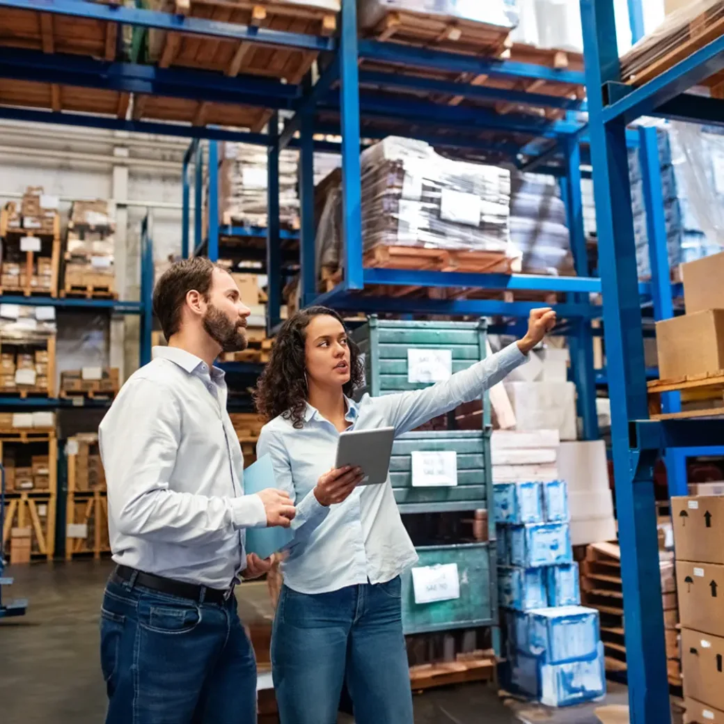 Businesswoman with a digital tablet showing and talking with male worker in distribution warehouse. Manager working with foreman in warehouse checking stock levels.