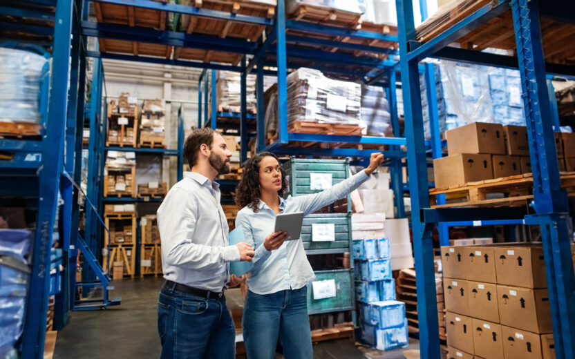 Businesswoman with a digital tablet showing and talking with male worker in distribution warehouse. Manager working with foreman in warehouse checking stock levels.