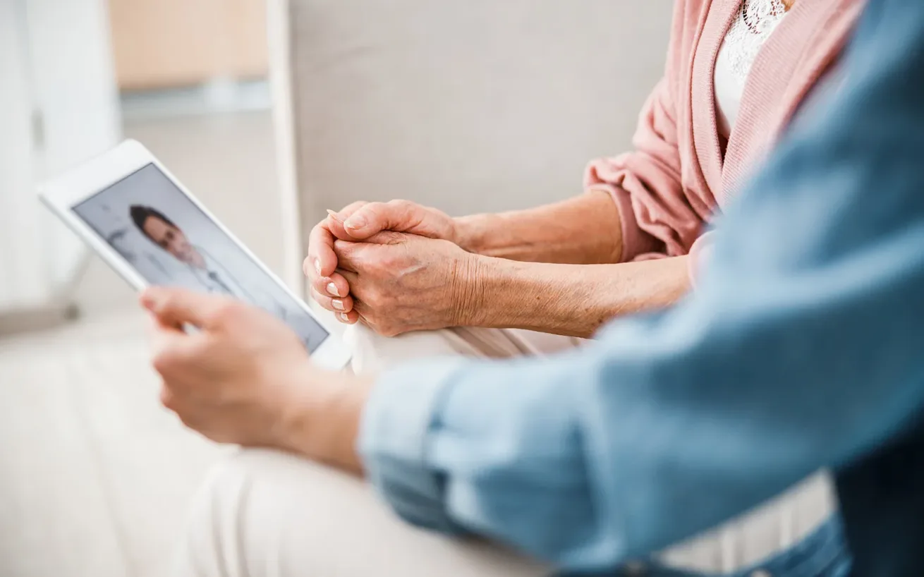 Image of a woman with an elderly lady holding a tablet and making a video call to a doctor