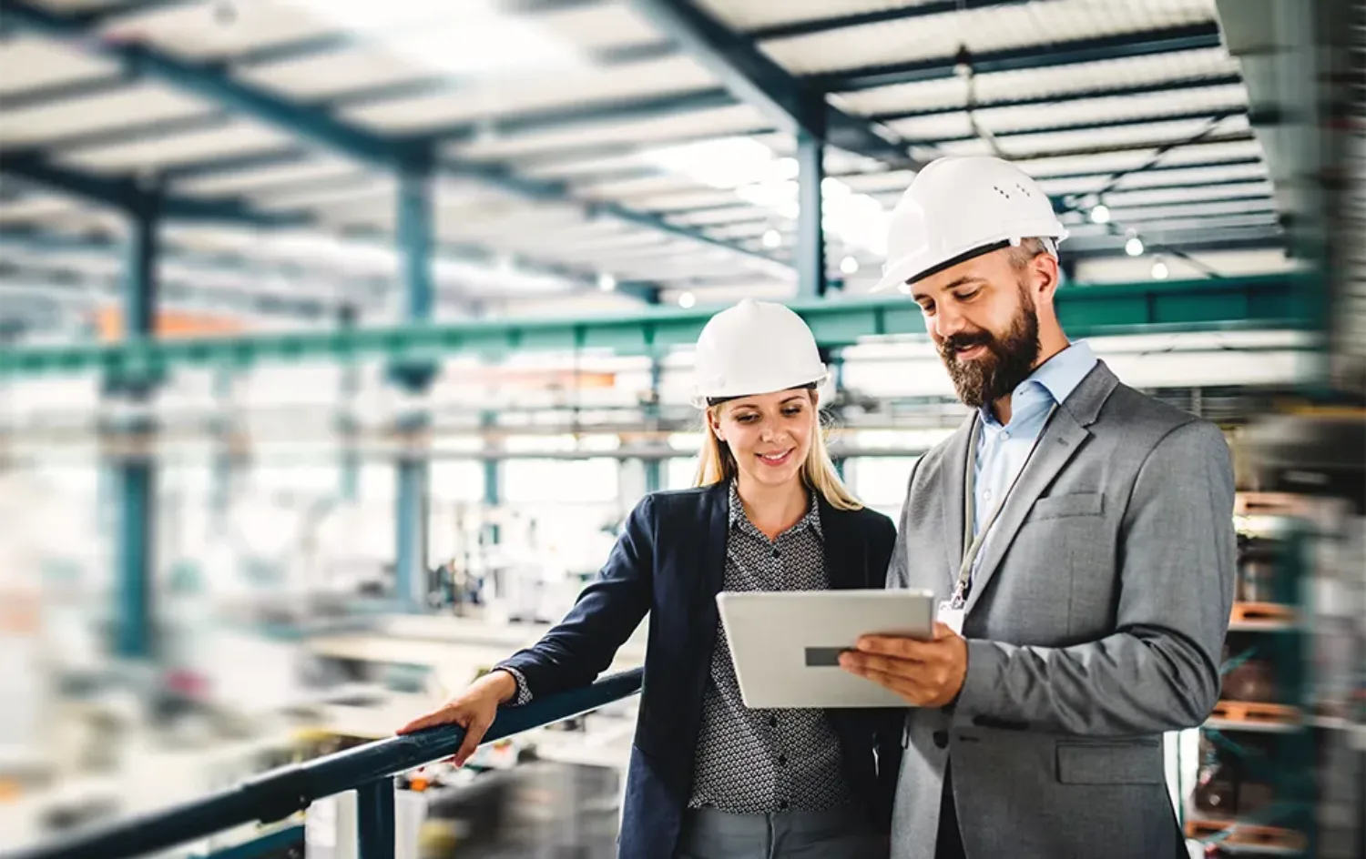 Woman and man standing on production site wearing safety helmets looking at mobile device