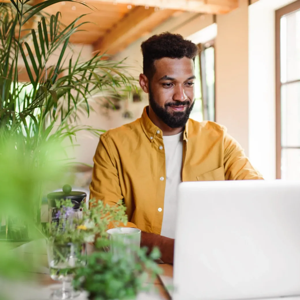 Young man with laptop and coffee working indoors, home office concept.