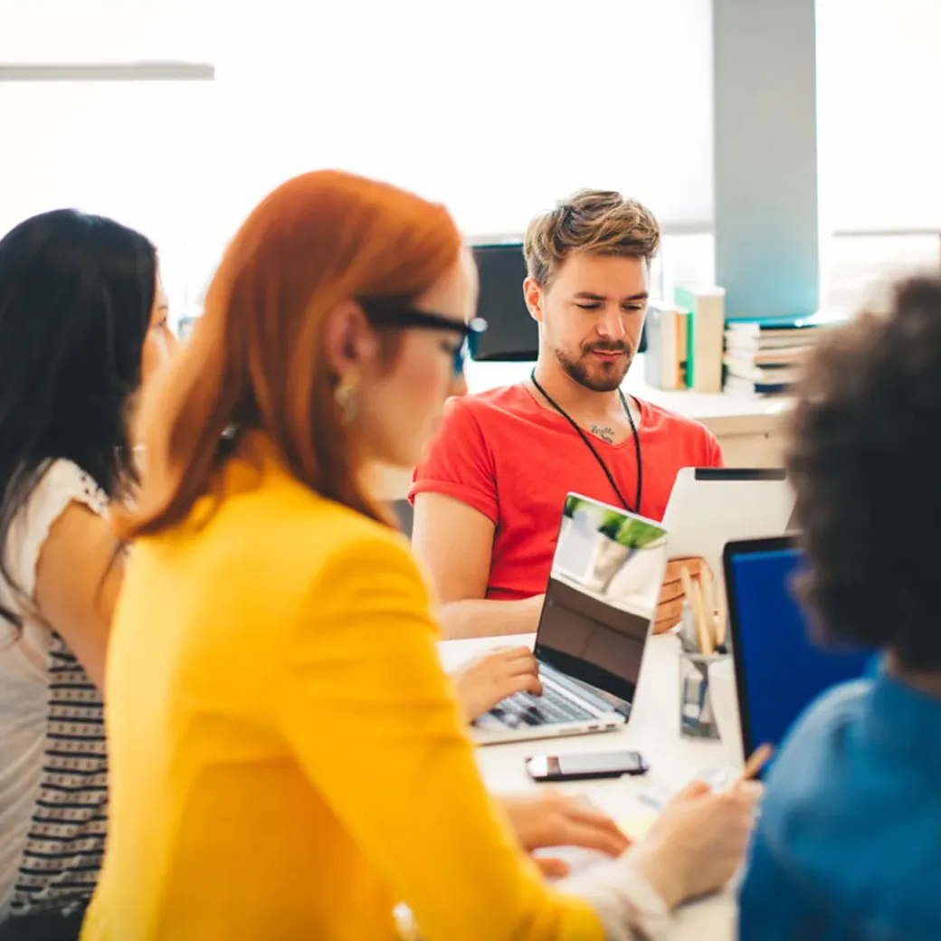 Start up team having a meeting in the office and planning a new project. Sitting by the table, using laptops, digital tablets, notes. Talking and brainstorming. Multi-Ethnic Group.Wearing casual clothes. | Training Center