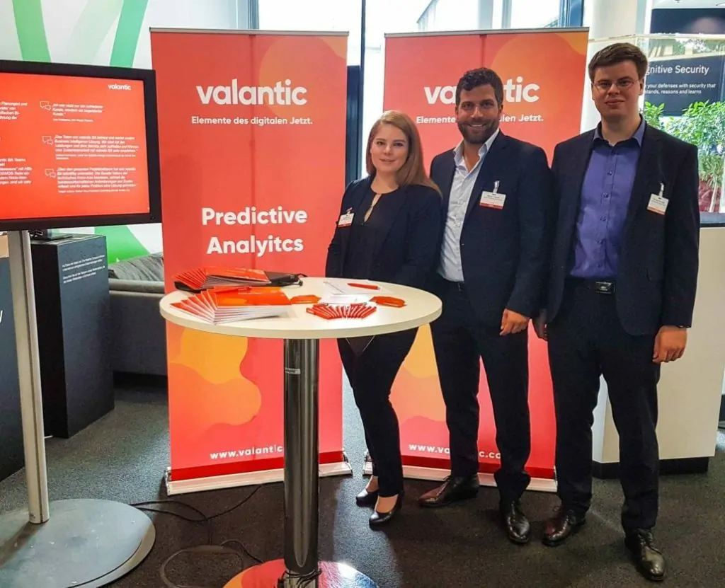 Bild von drei Personen an einem Messestand, Das valantic Team präsentiert als Aussteller und Sponsor auf dem TM1 / Planning Analytics Anwendertag in Stuttgart seine Cognitive Analytics und Predictive Analytics Lösungen.