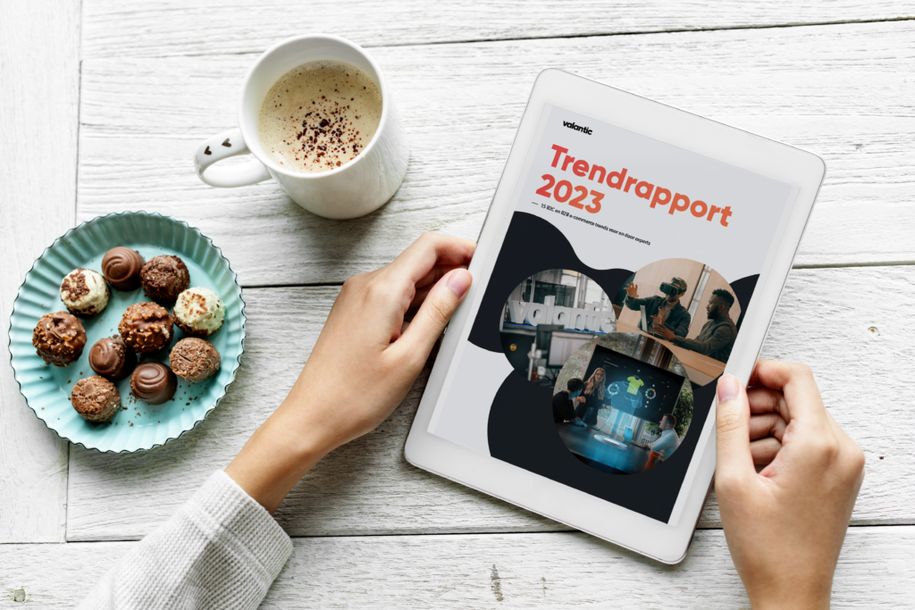 een tablet ligt op een tafel, het valantic trendrapport 2023 is geopend en er staat koffie en chocolade naast.