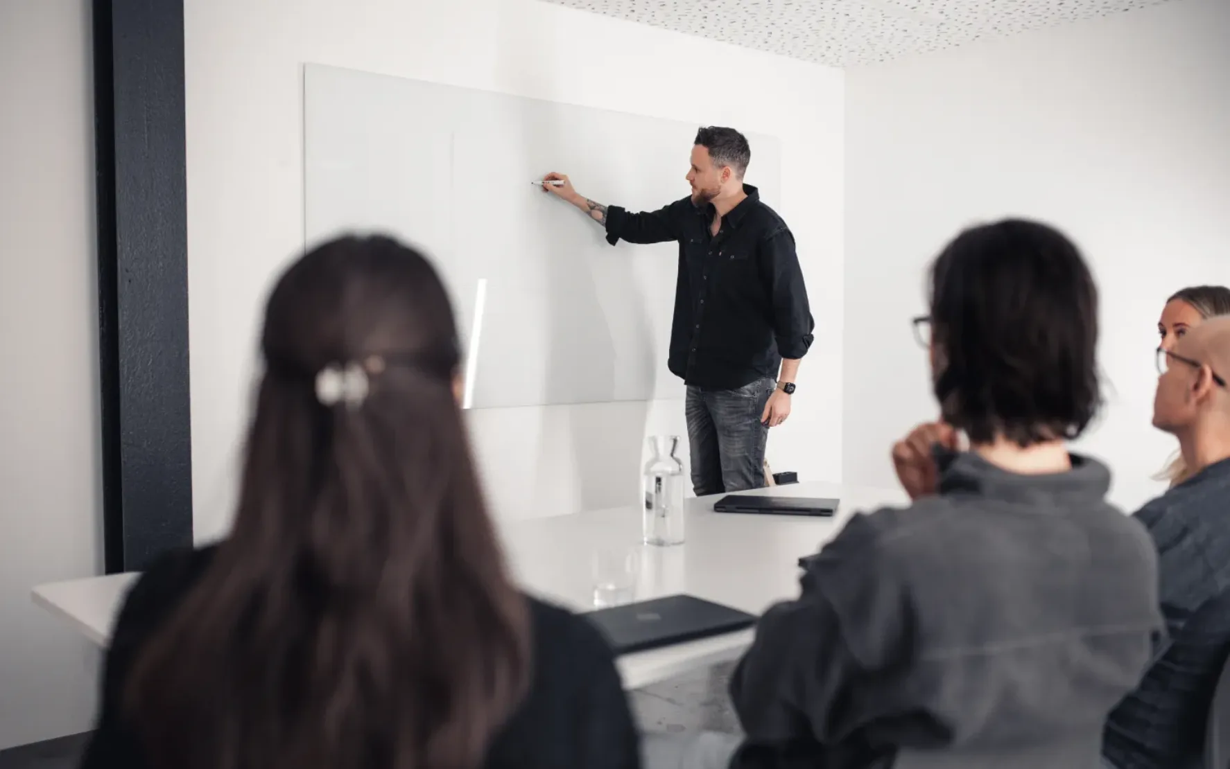 Ein Mann zeichnet an ein White Board, während vier Kollegen ihm zuhören.