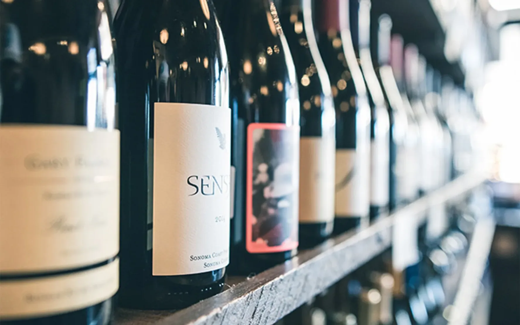 Nahaufnahme mehrerer Weinflaschen in einem Regal, Fokus auf das Etikett einer Flasche mit der Aufschrift „Sensi“.