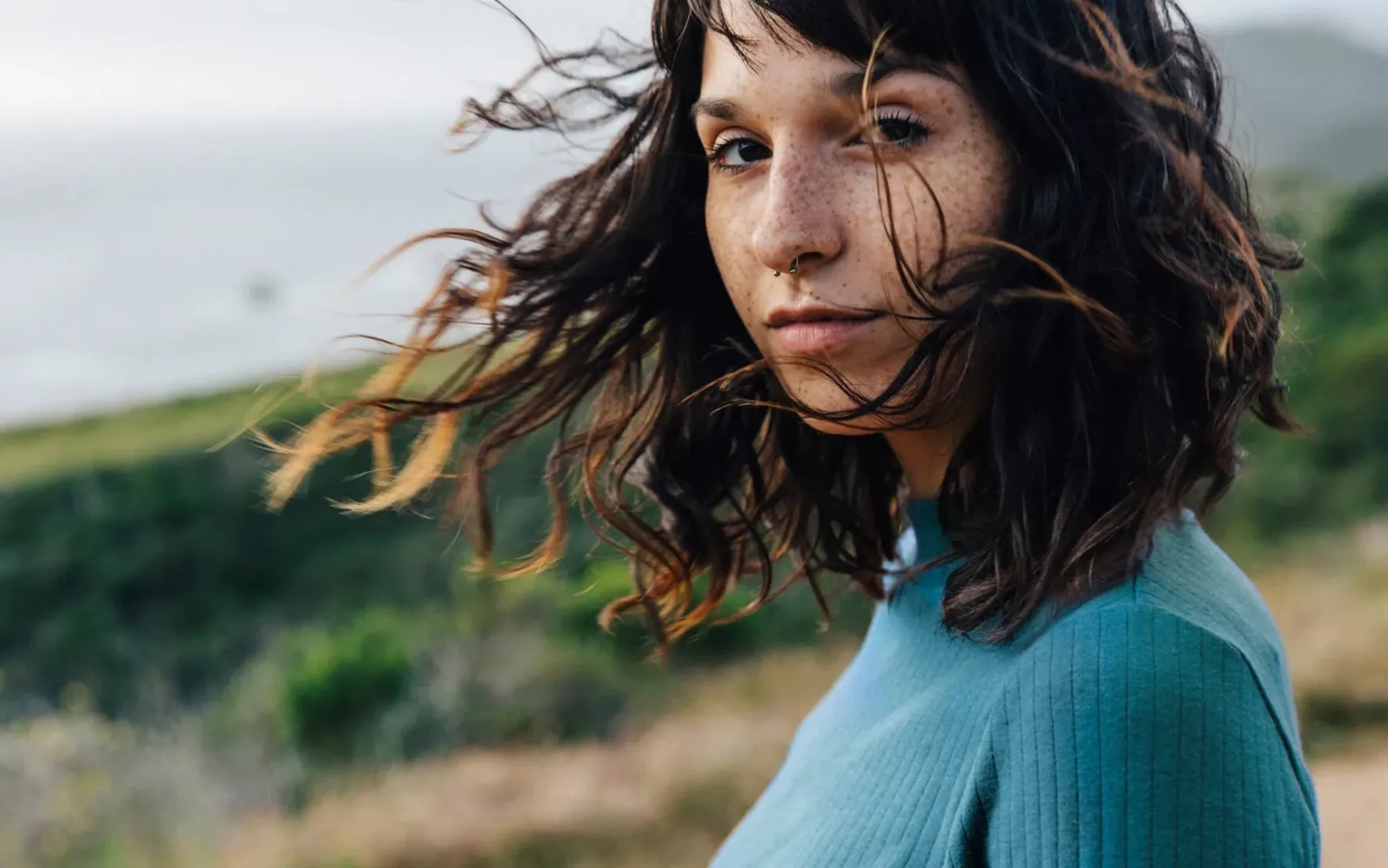 Porträt einer Person mit dunklen Haaren im Wind, im Freien aufgenommen.