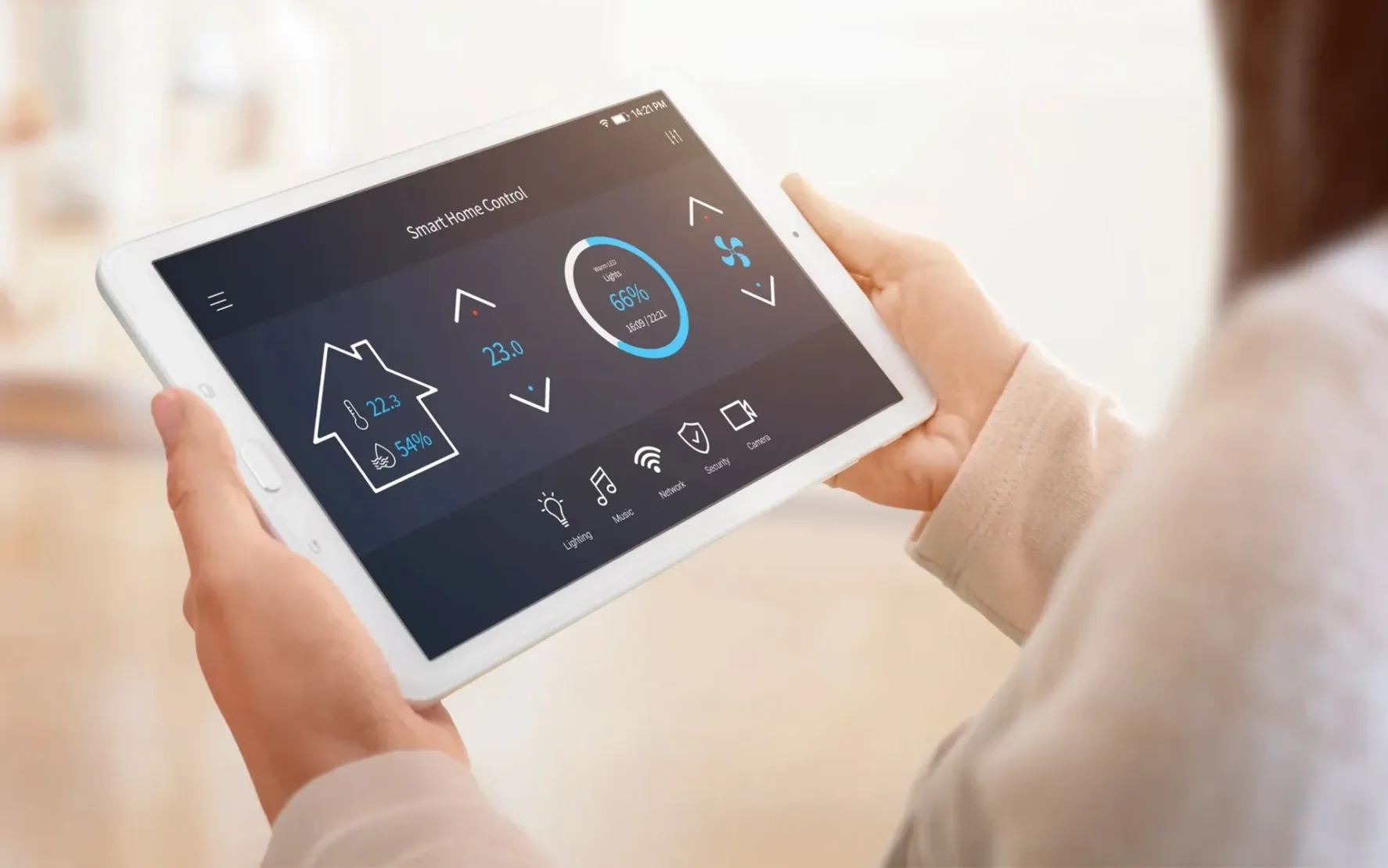 Person hält ein weißes Tablet mit Smart-Home-Dashboard; angezeigt sind Temperatur, ein 66 %-Kreis und Icons für Licht, Musik, Netzwerk, Sicherheit und Energie.