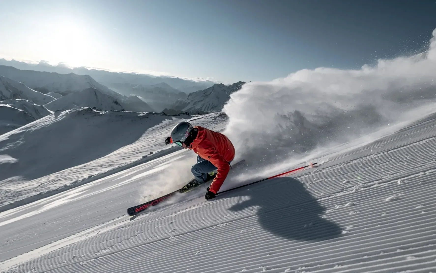 Skier in a red jacket carving down a freshly groomed slope, snow spraying up.